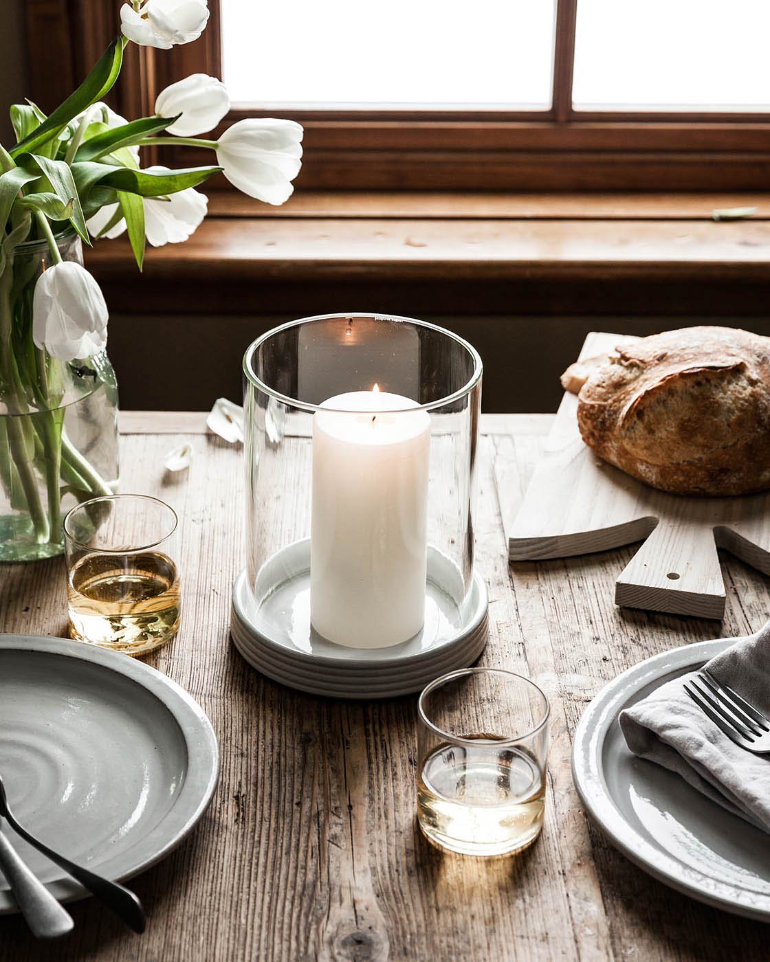 elegant hurricane candle holder shown on a rustic table with flowers and bread